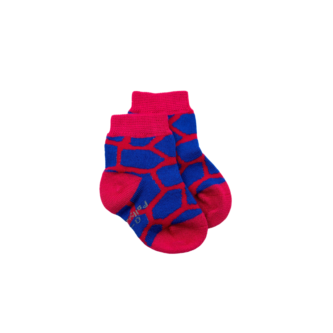 A pair of baby seamless bamboo crew socks featuring a bold blue and red giraffe-like abstract pattern, with solid red cuffs, toes, and heels, displayed against a plain white background.